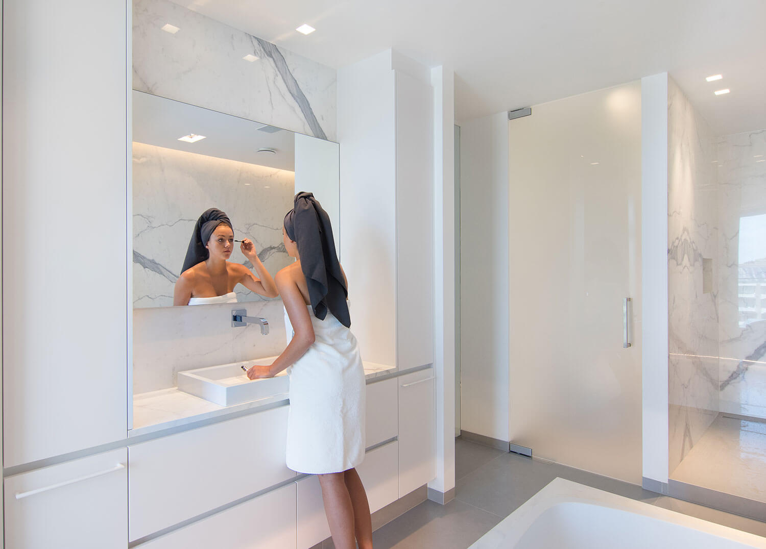 foto van dame die zich aan het opmaken is in een moderne badkamer met keramische tegels die de indruk van marmer geven.