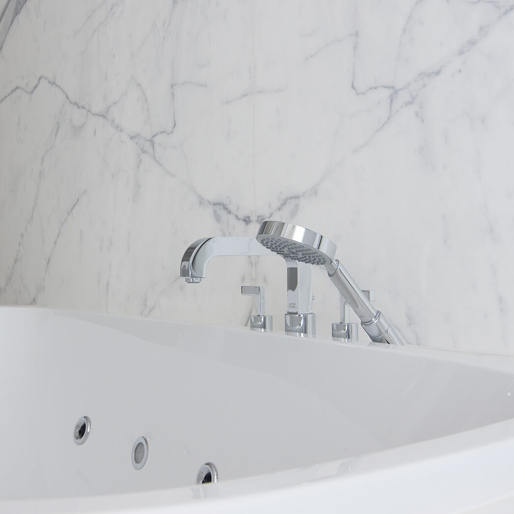 Detailfoto van kraan aan bad in moderne badkamer met keramische tegels die de indruk van marmer geven
