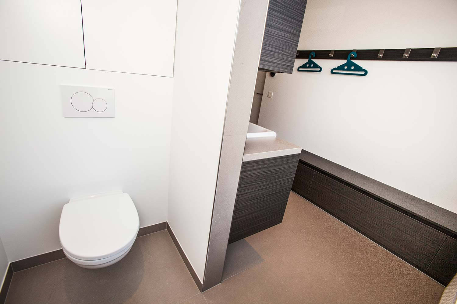 foto van een moderne badkamer, grijze tegels op de vloer, bruine kasten en kapstokken aan de muur