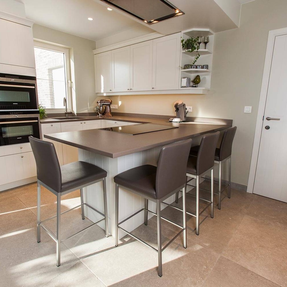 totaalzicht van keuken met witte kastjes, bruin-grijs werkblad en beige grote tegels op de vloer