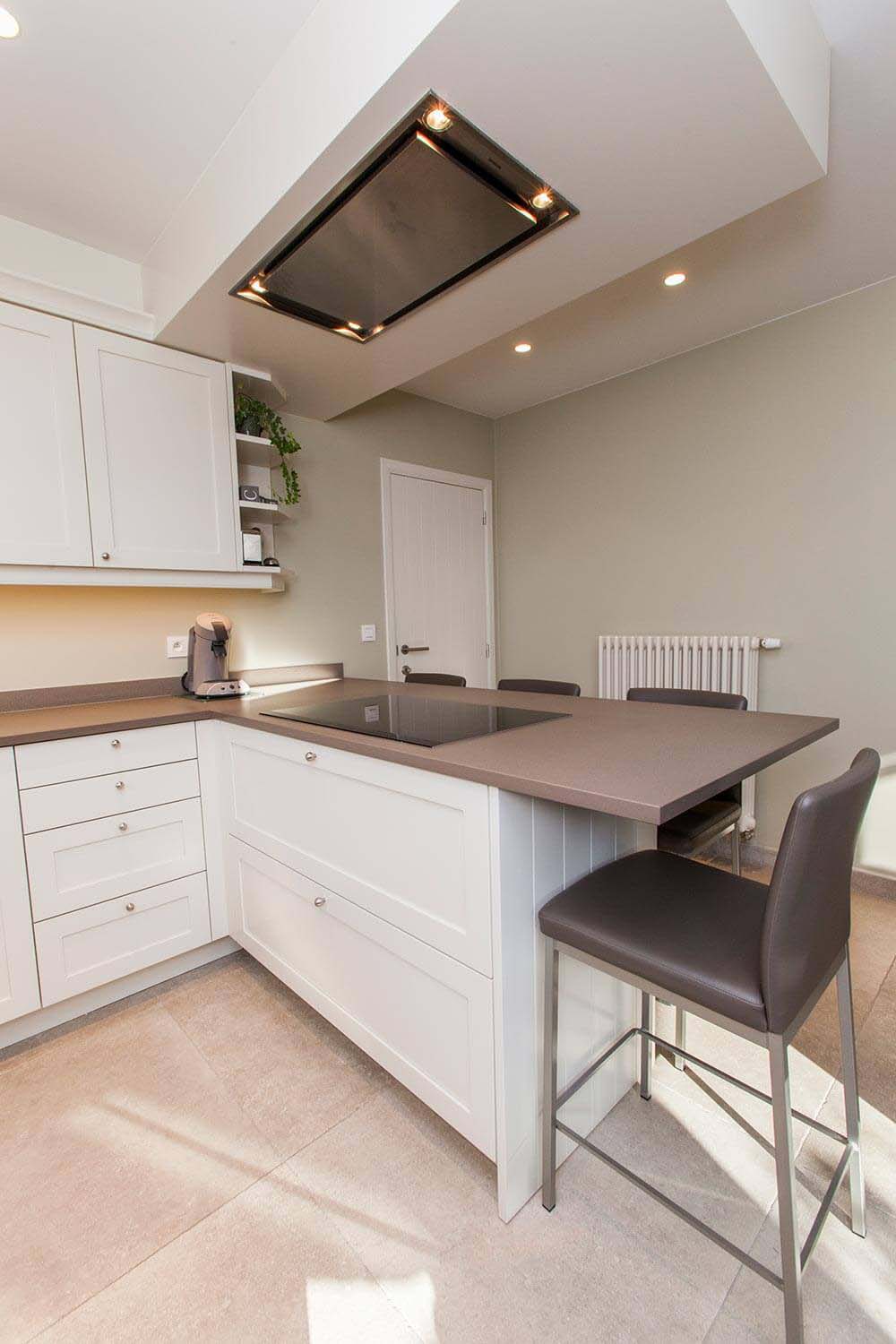 foto van keuken met ontbijtbar. Keuken met witte kastjes, beige tegels op de vloer en bruin-grijs werkblad