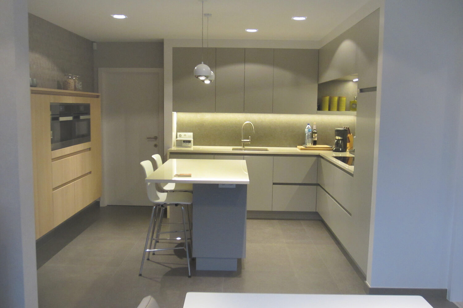 Totaaloverzicht van de keuken, rechts zijn er keukenkasten, het fornuis. Centraal een bartafel en links een ingebouwde kast met ingebouwde oven